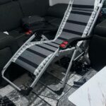 Foldable Full Recliner Lawn Chair in a reclining position on a grassy outdoor surface with adjustable armrests and cup holder.